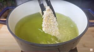 Panko-coated chicken breast being lowered into hot oil in a pot for frying.